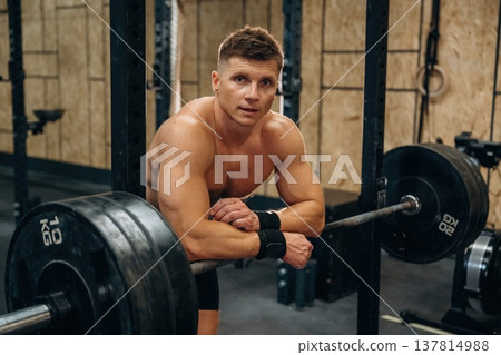 Time for the rest, standing and leaning on the barbell. Athletic man is in a gym 137814988