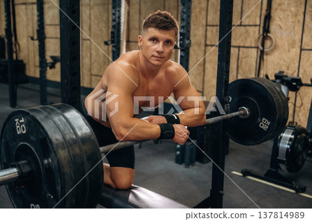 Time for the rest, standing and leaning on the barbell. Athletic man is in a gym 137814989