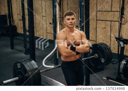 Break, posing. Athletic man performing weightlifting exercises with a barbell in a gym Break, posing. Athletic man performing weightlifting exercises with a barbell in a gym 137814998