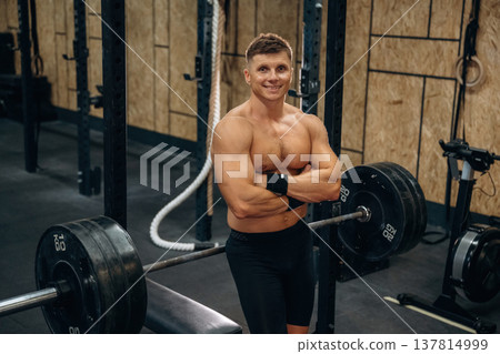 Break, posing. Athletic man performing weightlifting exercises with a barbell in a gym Break, posing. Athletic man performing weightlifting exercises with a barbell in a gym 137814999