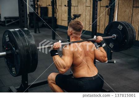 Squats with heavy barbell. Athletic man performing weightlifting exercises in a gym Squats with heavy barbell. Athletic man performing weightlifting exercises in a gym 137815001