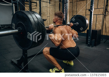 Squats with heavy barbell. Athletic man performing weightlifting exercises in a gym 137815003