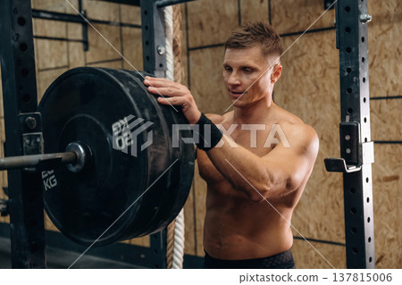 Athletic man performing weightlifting exercises with a barbell in a gym 137815006