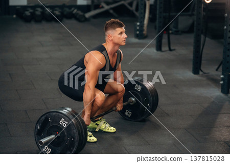 Sitting, ready for squats. Athletic man performing weightlifting exercises with a barbell in a gym 137815028