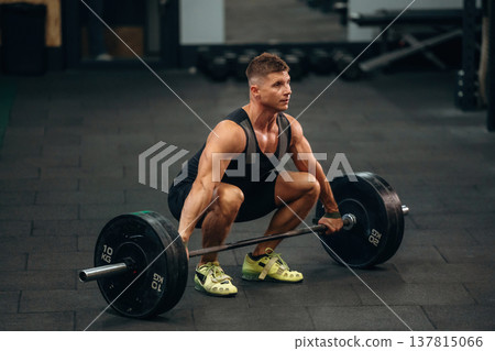 Performing weightlifting exercises with a barbell. Athletic man is in a gym 137815066