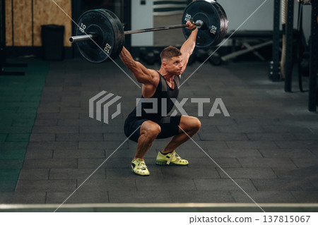 Performing weightlifting exercises with a barbell. Athletic man is in a gym 137815067