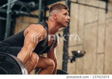 Side view. Athletic man performing weightlifting exercises with a barbell in a gym 137815074
