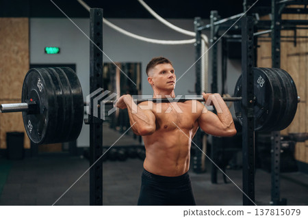 Strong muscular body. Holding a barbell. Athletic man performing weightlifting exercises in a gym Strong muscular body. Holding a barbell. Athletic man performing weightlifting exercises in a gym 137815079