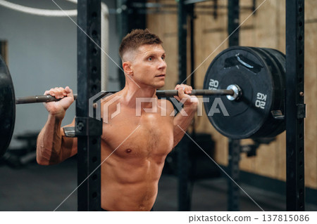 Performing weightlifting exercises with a barbell. Athletic man is in a gym 137815086