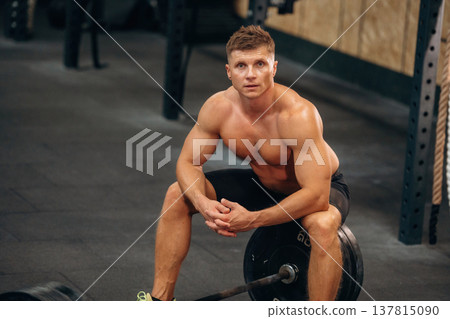 Athletic man performing weightlifting exercises with a barbell in a gym 137815090