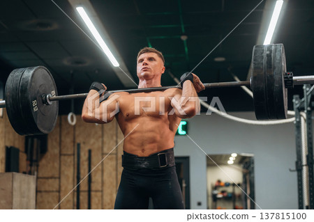 Focused on right technique. Athletic man performing weightlifting exercises with a barbell in a gym Focused on right technique. Athletic man performing weightlifting exercises with a barbell in a gym 137815100