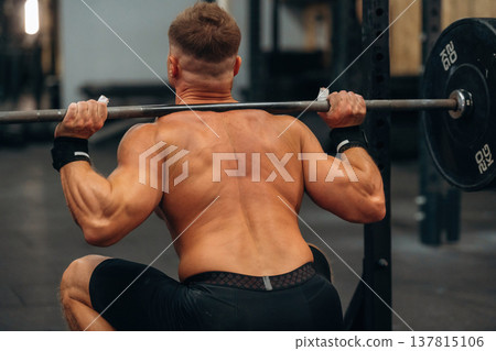 Barbell is on the neck and in hands. Athletic man performing weightlifting exercises in a gym Barbell is on the neck and in hands. Athletic man performing weightlifting exercises in a gym 137815106