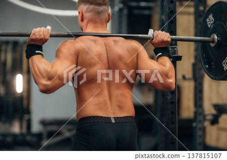 Barbell is on the neck and in hands. Athletic man performing weightlifting exercises in a gym Barbell is on the neck and in hands. Athletic man performing weightlifting exercises in a gym 137815107