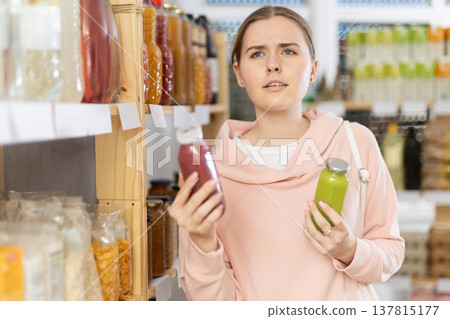 Girl customer in supermarket examines smoothie, chooses food-stuff in health lifestyle store Girl customer in supermarket examines smoothie, chooses food-stuff in health lifestyle store 137815177