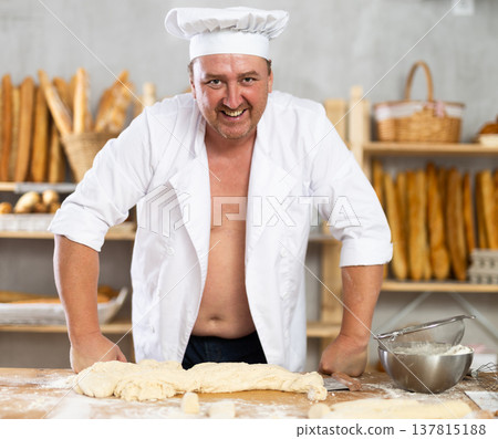 Male baker in unbuttoned uniform prepares dough, kneads it with his hands Male baker in unbuttoned uniform prepares dough, kneads it with his hands 137815188