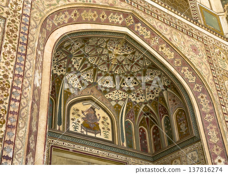 Jaipur palace arch displays colorful mural and intricate floral ornament across vaulted ceiling. 137816274