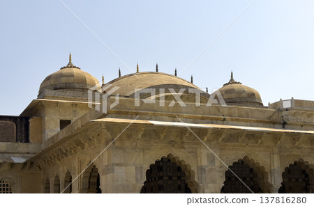 Jaipur palace rooftop features sandstone dome and ornate arch facade beneath clear sky. Historic 137816280
