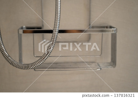 Chrome shower caddy with a flexible metal shower hose against a light bathroom wall, providing essential storage and organization for shower essentials 137816321