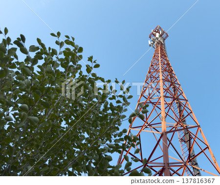 Telecommunication tower rises against blue sky with steel lattice structure and antenna equipment on 137816367