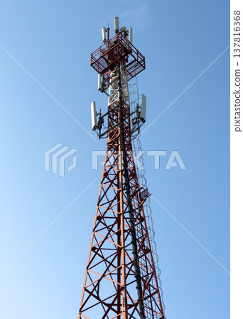 Telecommunication tower with antenna and wireless network equipment rises against blue sky. Red 137816368