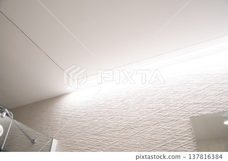 Modern bathroom interior showing minimalist aesthetic with textured wall tiles and a contemporary linear LED lighting fixture illuminating the space Modern bathroom interior showing minimalist aesthetic with textured wall tiles and a contemporary linear LED lighting fixture illuminating the space 137816384