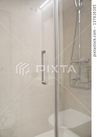 Interior view of a contemporary shower cabin showcasing a clear glass door with sleek metal handle against neutral tiled walls, providing a sense of comfort and refreshing hygiene Interior view of a contemporary shower cabin showcasing a clear glass door with sleek metal handle against neutral tiled walls, providing a sense of comfort and refreshing hygiene 137816385