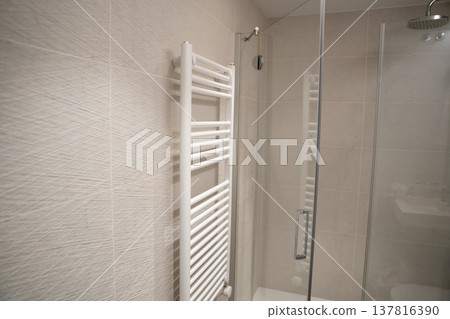 White towel rail radiator next to a modern glass shower enclosure with neutral textured tiles, creating a clean and functional interior bathroom design 137816390