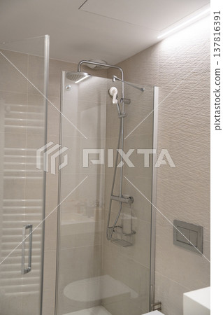 Modern bathroom interior showcasing a minimalist shower enclosure with a rain showerhead, handheld fixture, and textured wall tiles, offering a functional and elegant design 137816391
