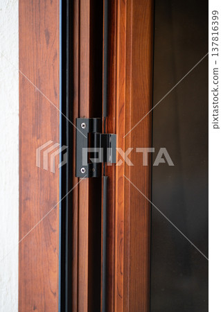Black metal door hinge attaching a dark wooden frame to a white wall, providing security and functionality for residential or commercial buildings Black metal door hinge attaching a dark wooden frame to a white wall, providing security and functionality for residential or commercial buildings 137816399