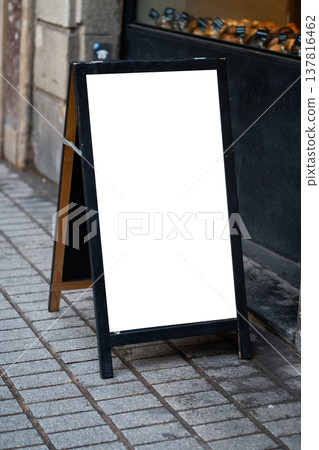 Blank sandwich board sign with white copy space mockup standing on a city sidewalk pavement, advertising specials for a local bakery or cafe storefront business 137816462