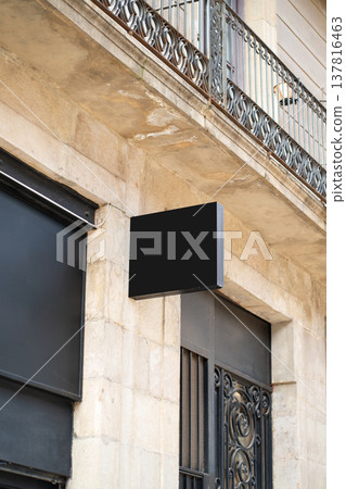 Black rectangular blank store sign mockup providing space for retail branding, business advertising, or custom text on a stone building facade below an ornate balcony railing Black rectangular blank store sign mockup providing space for retail branding, business advertising, or custom text on a stone building facade below an ornate balcony railing 137816463