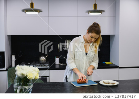 Woman slicing sausage for sandwich in modern kitchen Woman slicing sausage for sandwich in modern kitchen 137817417