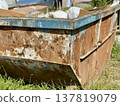 An Old and Rusty Dump Container That is Surrounded by Lush, Overgrown Grass and Weeds. A weathered metal dumpster overflowing with various debris, positioned against a backdrop of lush tall grass. 137819079