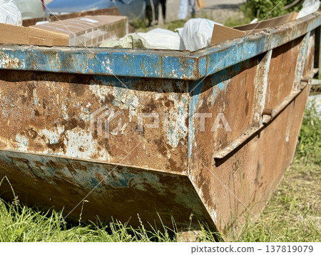 An Old and Rusty Dump Container That is Surrounded by Lush, Overgrown Grass and Weeds. A weathered metal dumpster overflowing with various debris, positioned against a backdrop of lush tall grass. 137819079