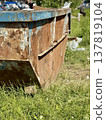 An Old and Rusty Dump Container That is Surrounded by Lush, Overgrown Grass and Weeds. A weathered metal dumpster overflowing with various debris, positioned against a backdrop of lush tall grass. 137819104