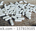 Numerous white capsules scattered over the textured surface create an artistic effect. A close-up of various white capsules for the treatment of human health is shown. 137819105