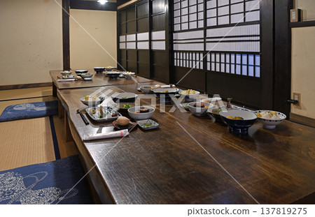 A scene of a traditional Japanese dinner in a renovated old house, featuring flavorful autumn regional dishes and traditional Japanese cuisine laid out on a single-slab table. A scene of a traditional Japanese dinner in a renovated old house, featuring flavorful autumn regional dishes and traditional Japanese cuisine laid out on a single-slab table. 137819275