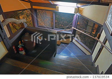 A heavy wooden staircase that evokes the history of the old house, and a view of the illuminated stone wall through the window. 137819534