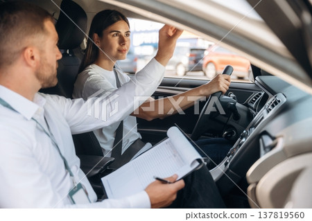 Data is being written into the notepad. Woman is with instructor in car, driving school concept 137819560