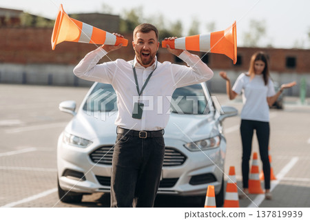 Fun by using cones. Man instructor in the driving school and woman are outside the car Fun by using cones. Man instructor in the driving school and woman are outside the car 137819939