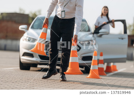 Placing the guide cones. Man instructor in the driving school and woman are outside the car 137819946