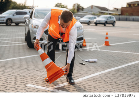 Putting the guidance cones at place. The road worker in orange uniform is with cones near car Putting the guidance cones at place. The road worker in orange uniform is with cones near car 137819972