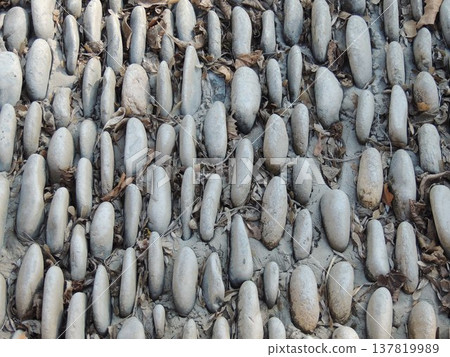 A textured background of round, solid stones set into hardened concrete as an exterior surface, the use of natural rock material in streetscape finishing, and cobblestones as a texture. A textured background of round, solid stones set into hardened concrete as an exterior surface, the use of natural rock material in streetscape finishing, and cobblestones as a texture. 137819989