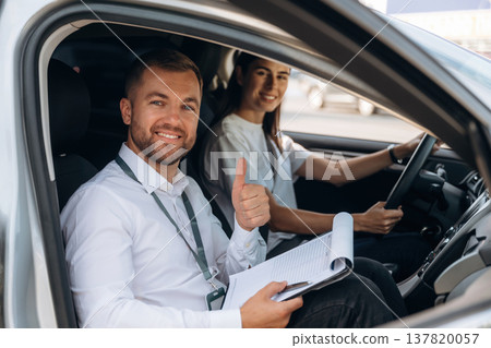 Gesture of thumb up, smiling. Woman is with instructor in car, driving school concept 137820057