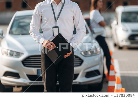 Documents in hands of a guy. Man instructor in the driving school and woman are outside the car 137820094