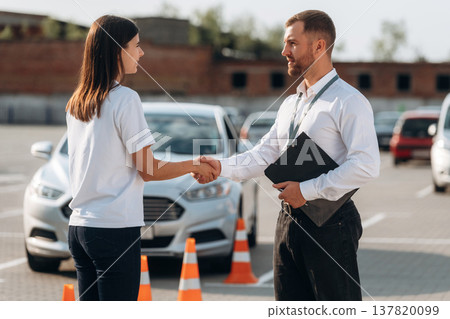 Shaking hands. Man instructor in the driving school and woman are outside the car Shaking hands. Man instructor in the driving school and woman are outside the car 137820099