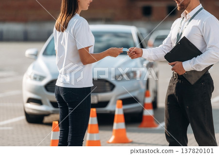 Giving the license, exam passed. Man instructor in the driving school and woman are outside the car 137820101