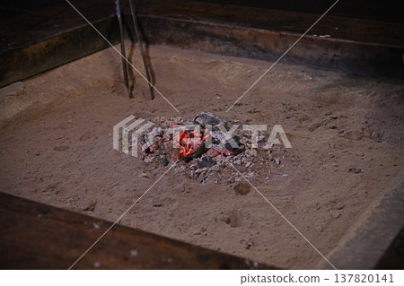 The glowing red charcoal fire in the hearth and the tranquil atmosphere of the old farmhouse create a traditional Japanese space. 137820141