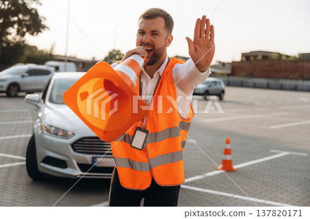 Talking into the cone, having fun. The road worker in orange uniform is with cones near car 137820171