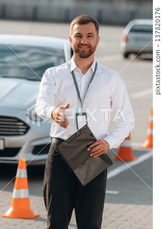 Driving school worker is outdoors near car 137820176